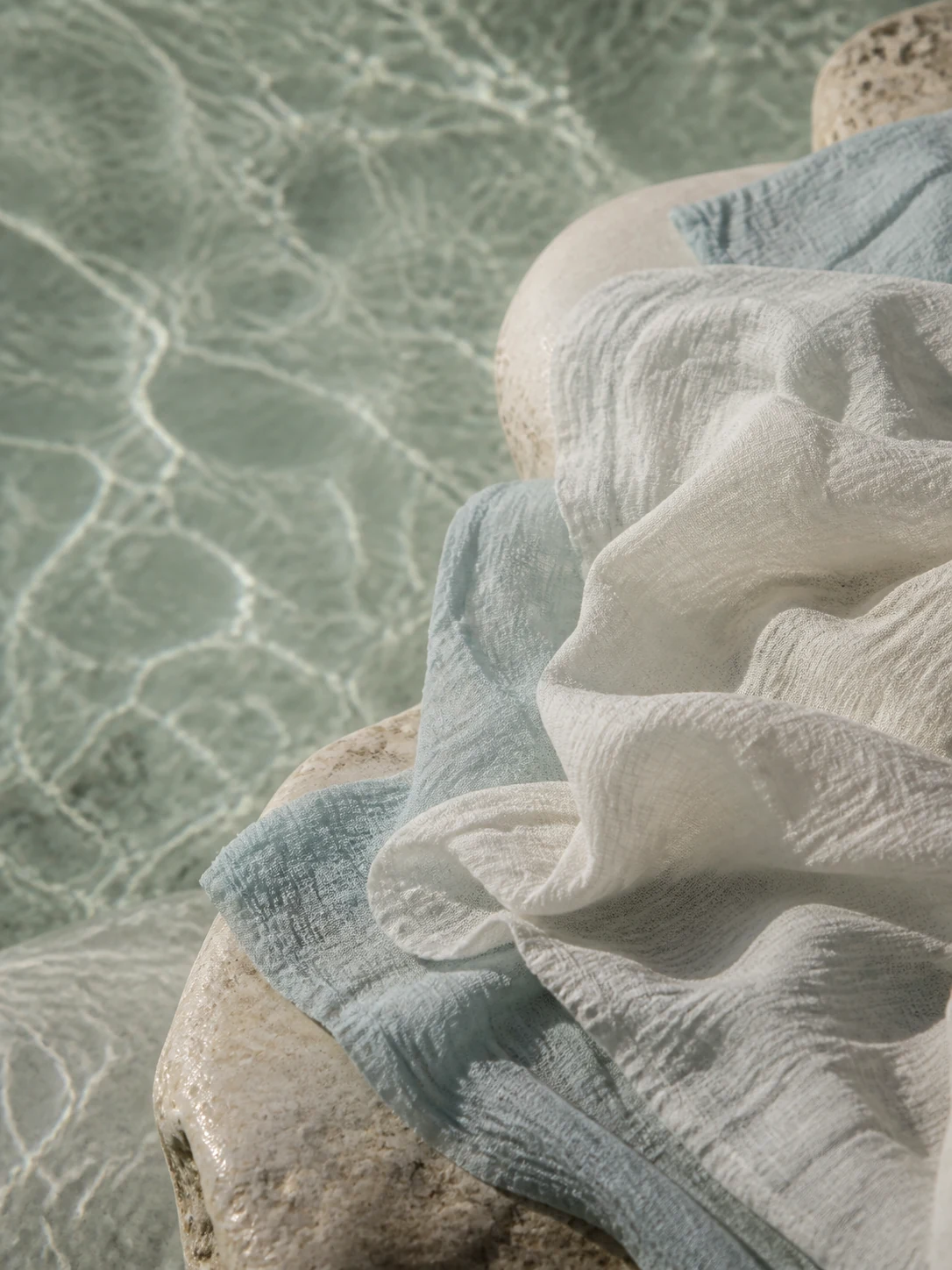 Crinkled natural cloth beside water in pale mineral tones